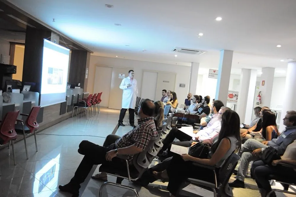 Médico de jaleco conduzindo uma apresentação para participantes sentados, no INCOR